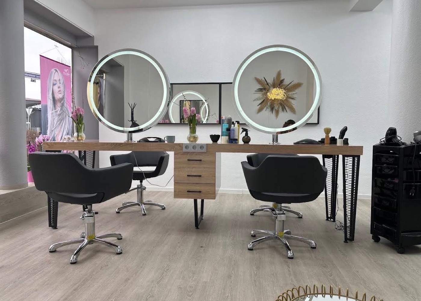 Heller Salon mit runden, beleuchteten Spiegeln und hellem Holz in der Heddernheimer Landstraße